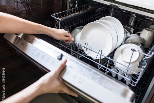Woman fill the used dish in dishwasher machine in kitchen at home.Hand of female holding the shelf.White clean dish or bowl and cup inside the washer device.Selective focus with blur background.