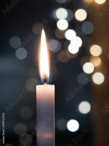Vertical closeup of a beautiful flaming candle with bokeh lights in the background