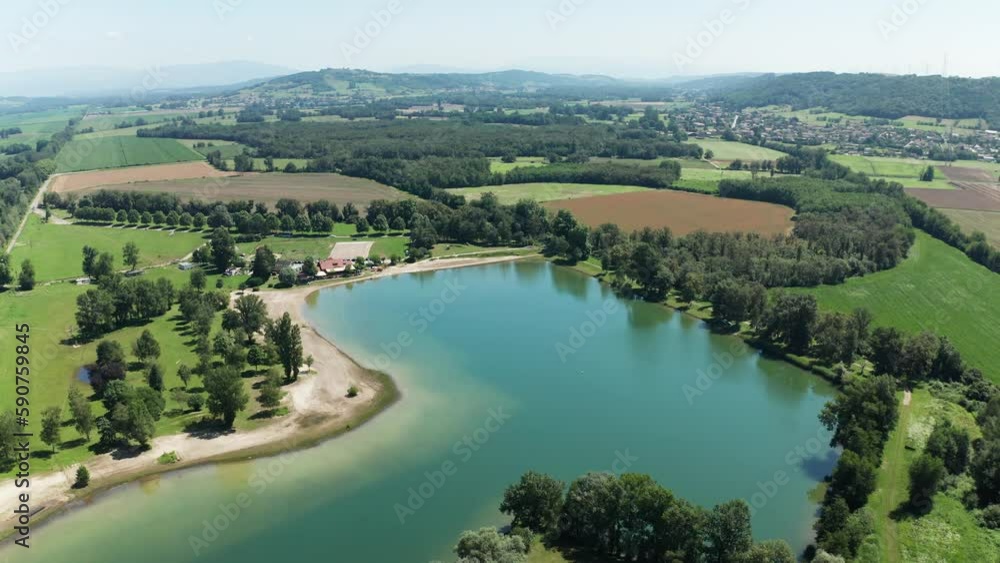 Aerial shot of a lake surrounded by vegetation and fields in a rural area in 4K Aerial shot of a lake surrounded by vegetation and fields in a rural area in 4K