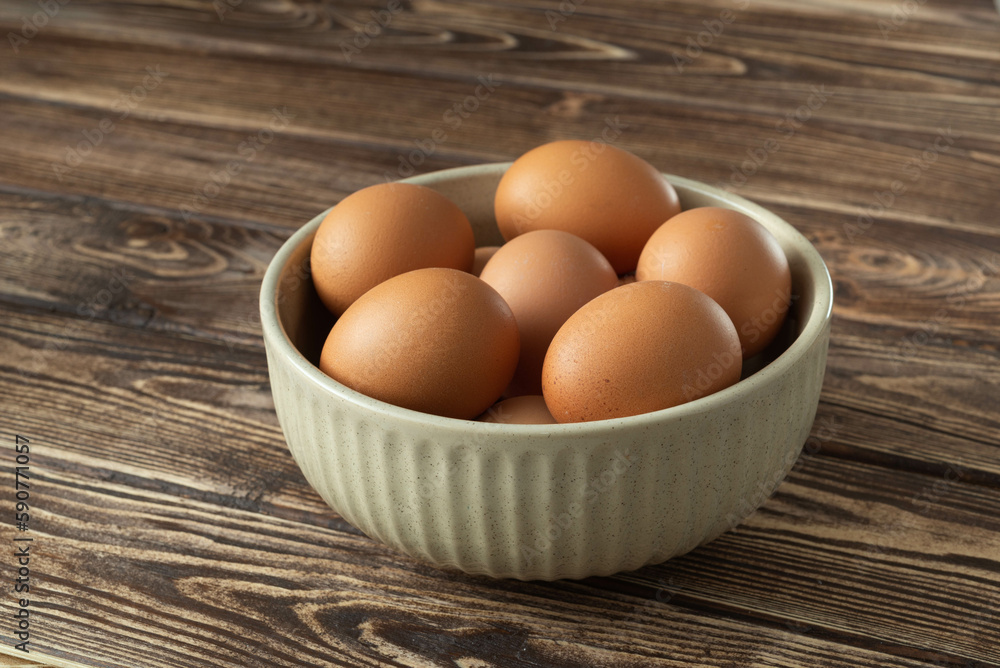 Uncooked eggs in a bowl on wooden background Uncooked eggs in a bowl on wooden background