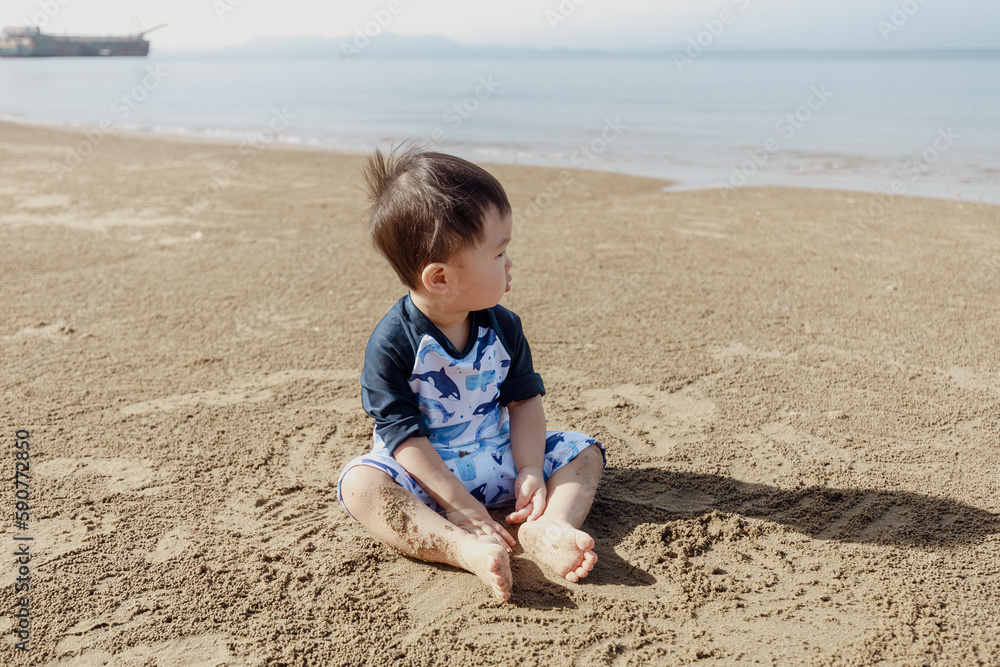 Child who is wearing the swimsuit is playing sand at beach Child who is wearing the swimsuit is playing sand at beach