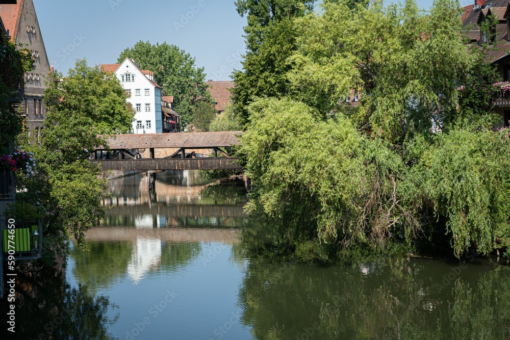 Bridge, trees, and buildings reflected on the Pegnitz river on a sunny day