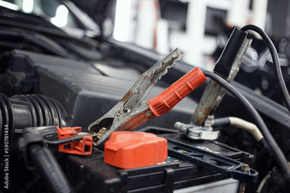 Close-up of a charging car battery with electricity using connecting cables, battery inspection. Selective focus. Blurred background.