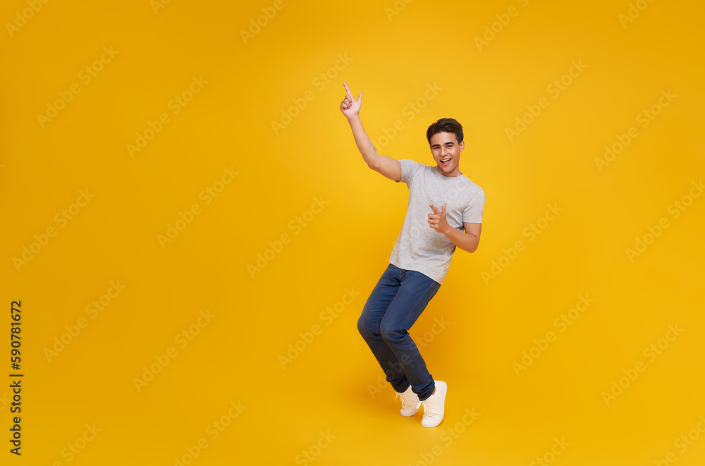 smiling handsome Asian man pointing fingers to empty space aside isolated on yellow studio background.