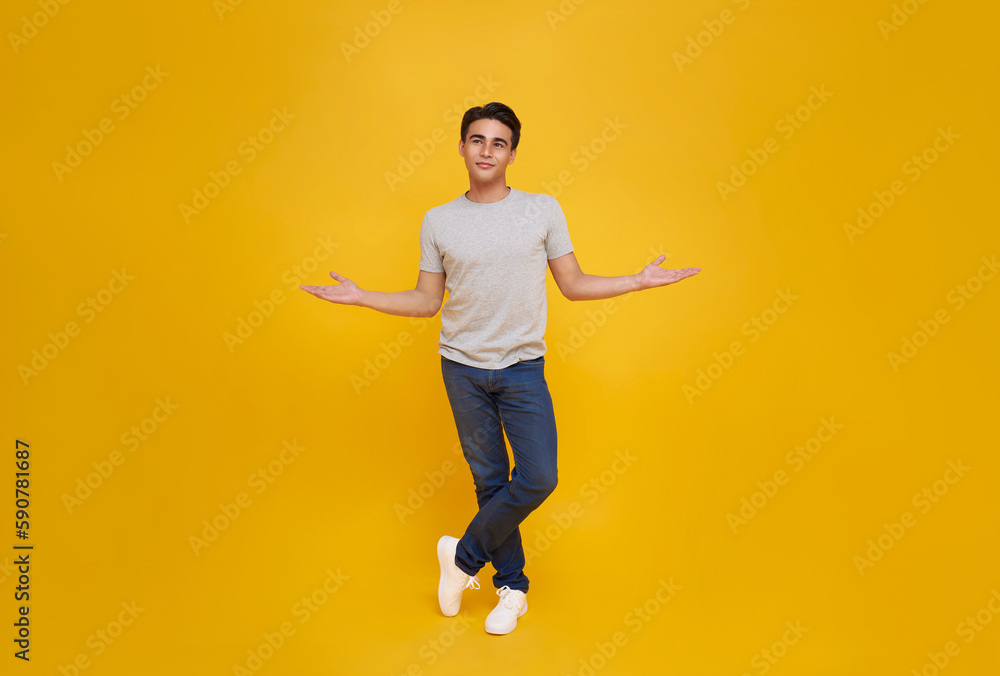smiling handsome Asian man looking upward and presenting or showing with open palms gesture isolated on yellow studio background.