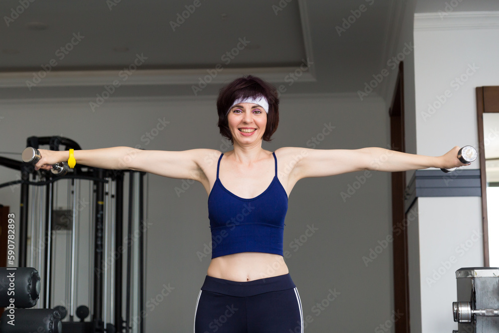 Girl in sportswear lifts dumbbells gym.