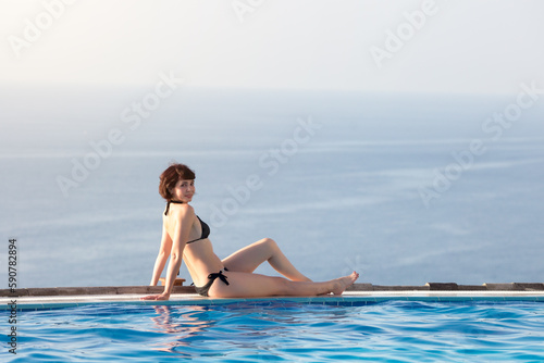Woman sunbathing nearpool in a luxury hotel overlooking ocean.