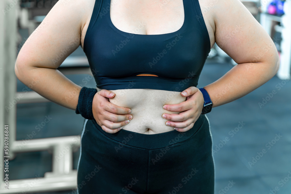 fat workout woman showing chubby belly before exercise. motivated exerciser  reveal fat under skin choosing training to burn calories. determined gym  member have spirit for changing unhealthy fat body Stock Photo