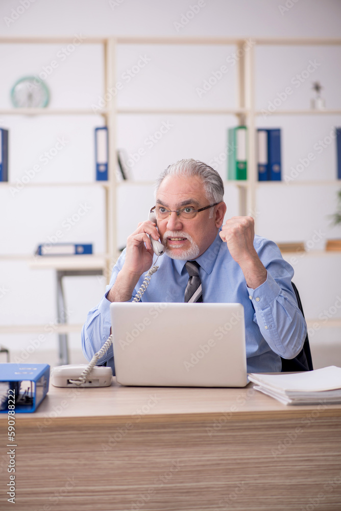 Old male employee speaking by phone in the office Old male employee speaking by phone in the office