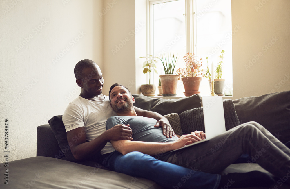 Multiracial smiling couple browsing laptop on sofa Multiracial smiling couple browsing laptop on sofa