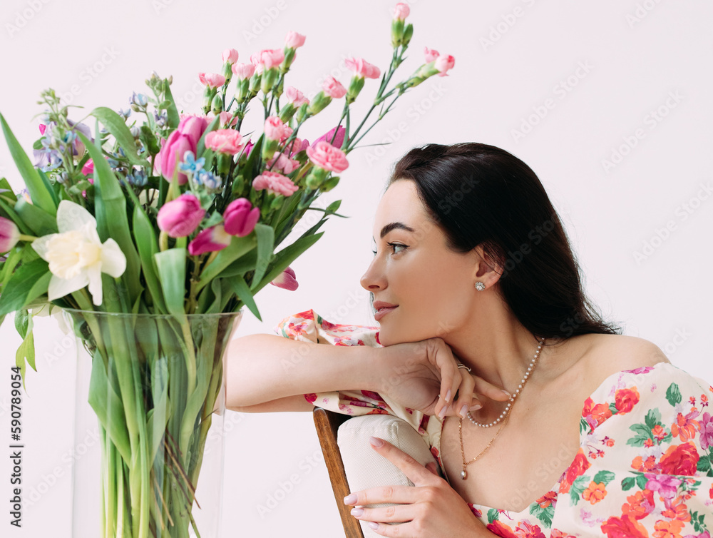Fototapeta premium Portrait of young happy woman near vase with flowers bouquet against white background.