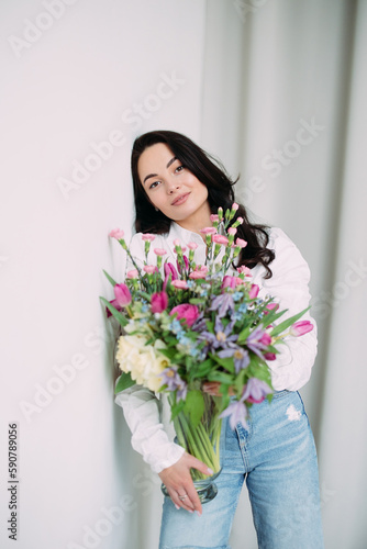 Young happy woman standing and holding vase with flowers bouquet in her hands.