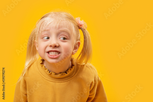 Portrait of preschooler blonde girl in yellow shirt on bright yellow background and smiling broadly. Empty space for advertising mockup