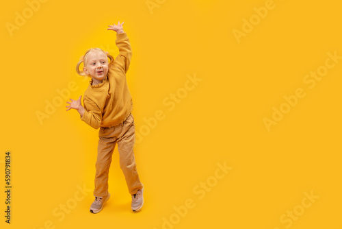 Full-length portrait of small blonde girl with two tails wears yellow clothes dance and poses. Copy space, mock up