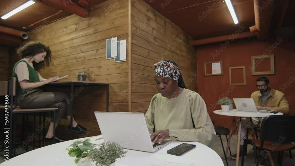 Full shot of casually dressed diverse male and female freelancers working at tables at loft-style shared workspace facility, typing on laptops and using tablet computer Full shot of casually dressed diverse male and female freelancers working at tables at loft-style shared workspace facility, typing on laptops and using tablet computer