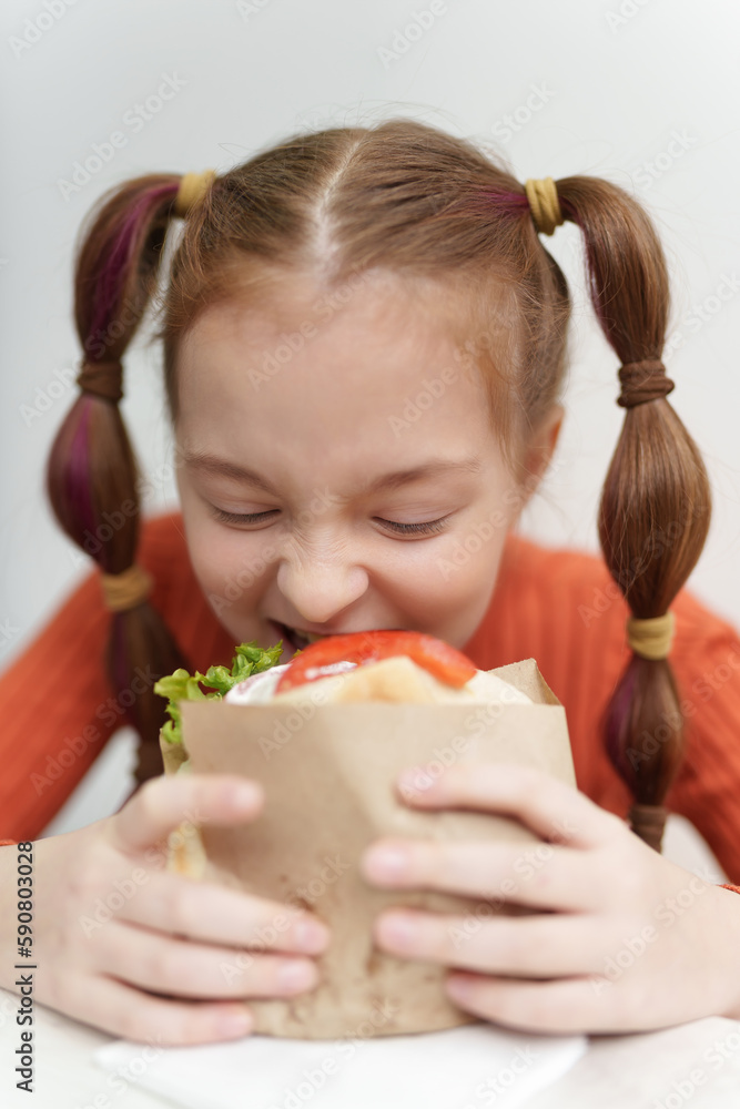Pretty white little girl with ponytails biting a sandwich. Portrait of cute elementary age kid eating Greek pita souvlaki in a fast food restaurant Pretty white little girl with ponytails biting a sandwich. Portrait of cute elementary age kid eating Greek pita souvlaki in a fast food restaurant