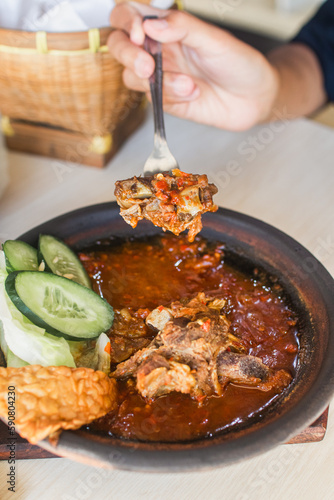Sambal iga or ribs with sambal cooked in earthenware plate against wooden background. Served on wooden table