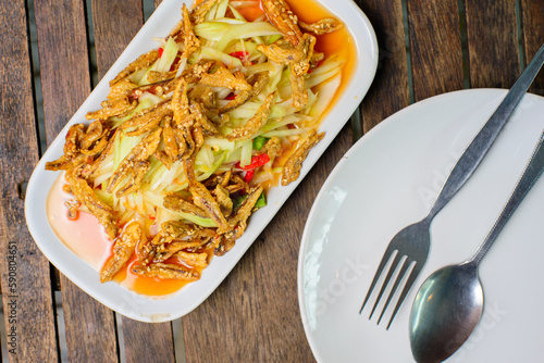 Spicy papaya salad with crispy fish on the wooden background.