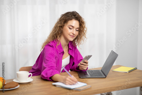 Beautiful Young Freelancer Woman Using Smartphone And Writing In Notepad © Prostock-studio