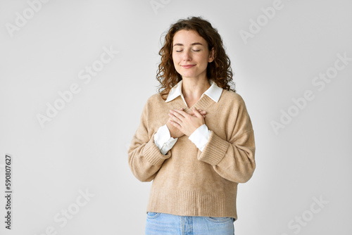 Happy pleased pretty young woman holding hands on chest feeling gratitude, mental balance, expressing thanking, kindness and love in heart standing isolated at white background.