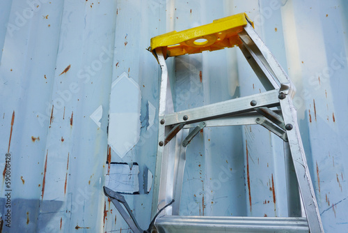 Aluminum folding ladder damaged (A-Type) is leaning against a container wall on construction site.
