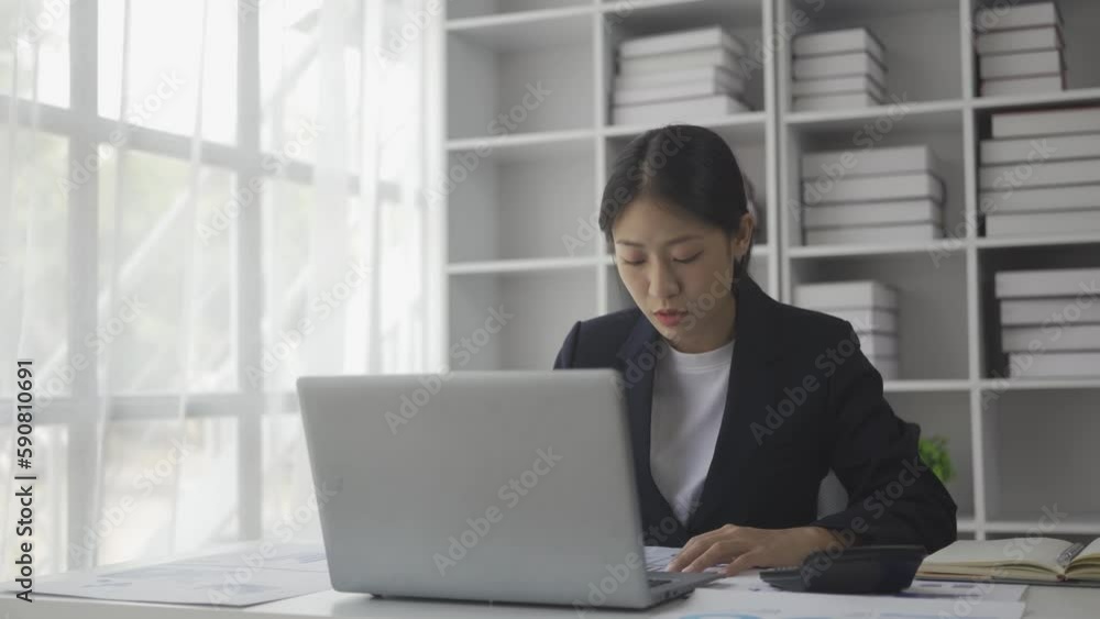Asian female accountant sitting at desk calculating monthly expenses using calculator checking utility bills managing family budget accountant working on paperwork Asian female accountant sitting at desk calculating monthly expenses using calculator checking utility bills managing family budget accountant working on paperwork