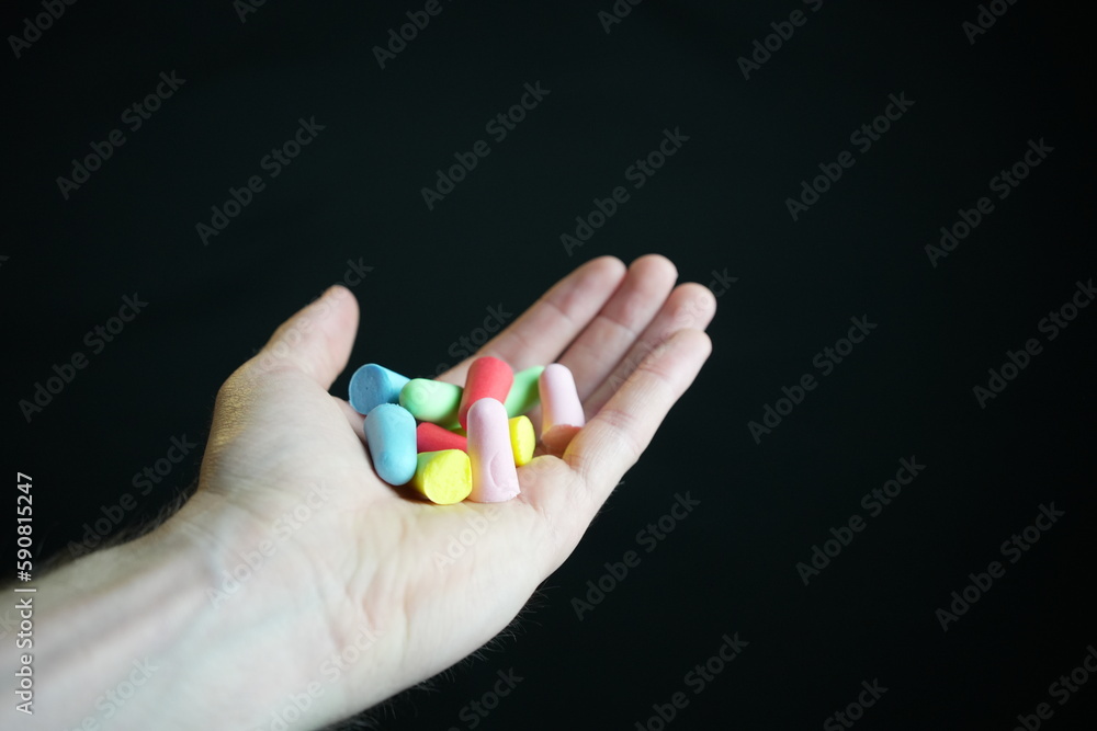 Hand holding colored earplugs, black background Hand holding colored earplugs, black background