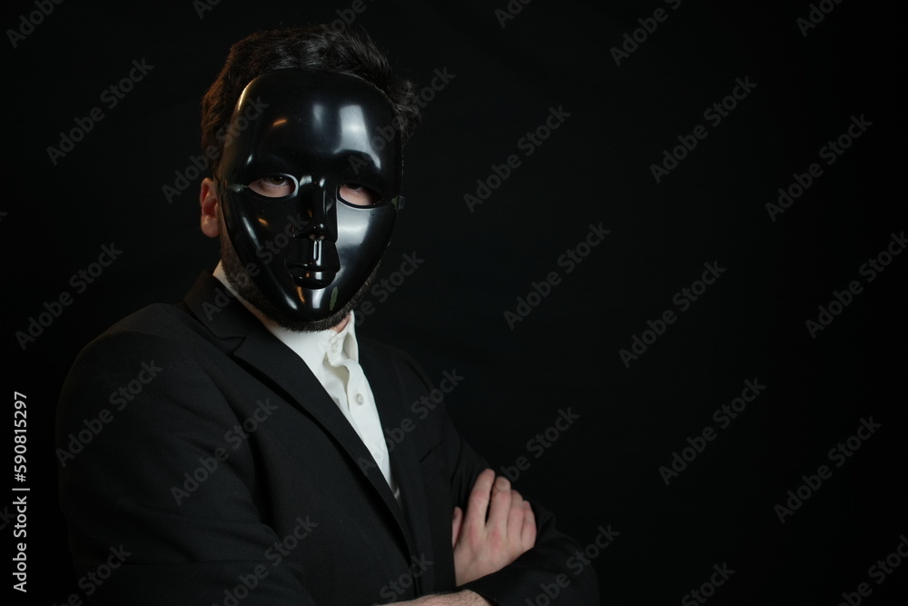 Elegant man on black background is wearing black plastic mask. Criminal hiding identity concept. Elegant man on black background is wearing black plastic mask. Criminal hiding identity concept.