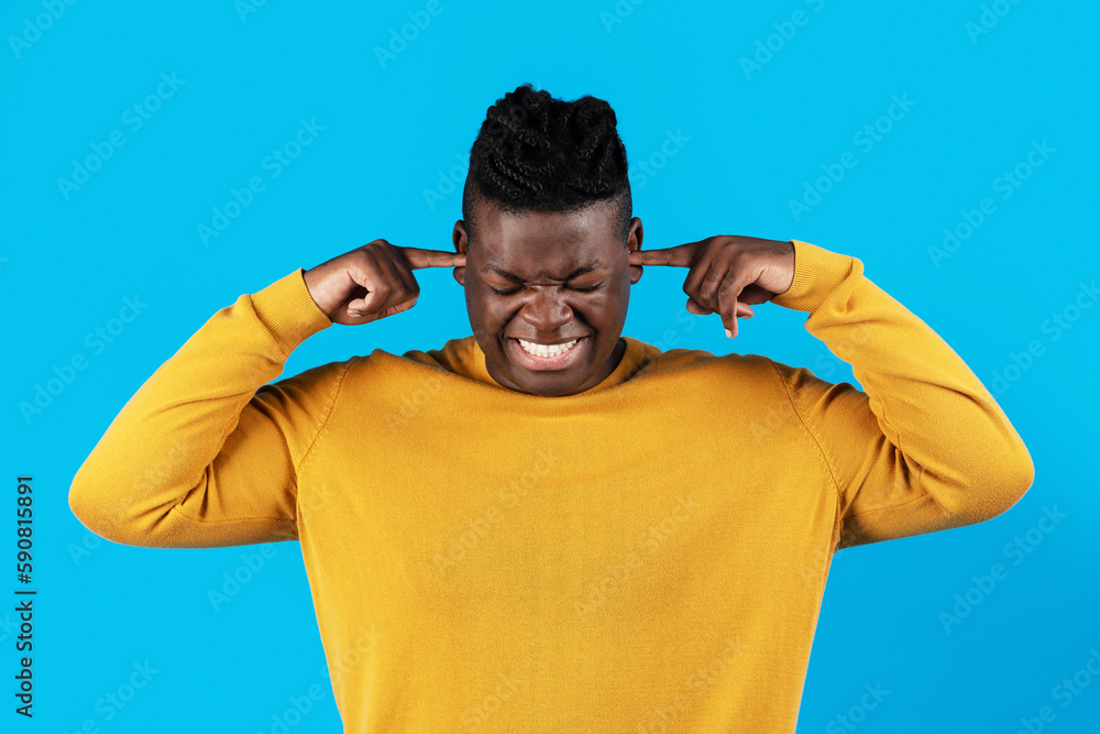 Naklejka premium Annoyed young african american man plugging ears with fingers over blue background