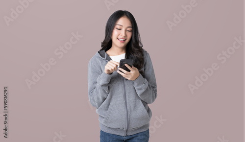 Young Asian woman texting message using mobile phone application on isolated brown background
