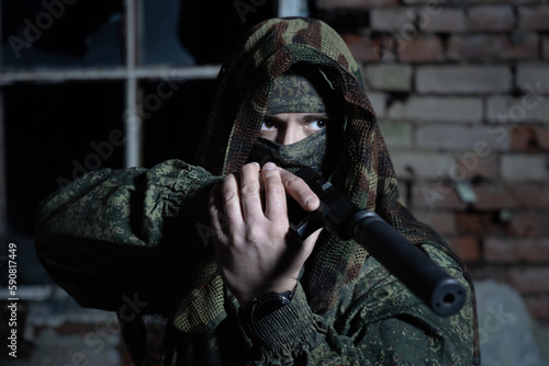Military intelligence officer in camouflage with a mask on his face with a pistol with a silencer in a dark room.