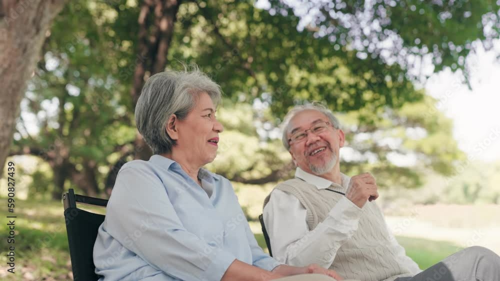 Senior Asian couple talking together and sitting on chair in a park during autumn morning
