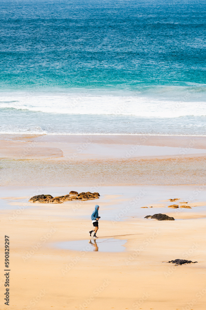 View from above, stunning aerial view of a person running on a beautiful beach bathed by the ocean and surrounded by beautiful sand dunes. Costa Calma, Fuerteventura, Canary Islands