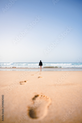 Stunning view a girl walking on the Cofete beach with her footprints on the sand in the foreground. Fuerteventura, Canary Islands.
