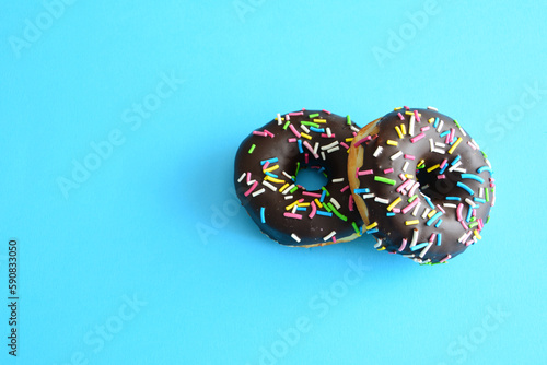 Two chocolate donuts with sprinkles on a blue background isolated, copy space 
