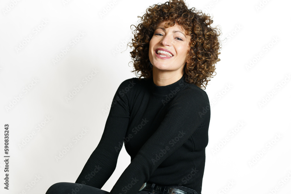 Smiling woman with curly hair sitting against white wall Smiling woman with curly hair sitting against white wall