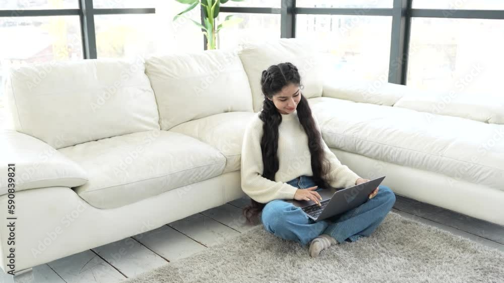 Beautiful young Indian woman student businesswoman sits on the floor leaning on couch and friendly chatting in messenger using laptop. Work and study from home in relaxed atmosphere. Natural light. Beautiful young Indian woman student businesswoman sits on the floor leaning on couch and friendly chatting in messenger using laptop. Work and study from home in relaxed atmosphere. Natural light.