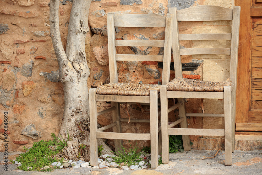 Monemvasia (Peloponnese, Greece) - Two wooden chairs and a tree trunk by the wall of a tenement house.