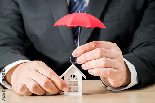 Photography Businessman hand hold open the red umbrella for protect to home model in the office, Loan or saving money for property protection  real estate and a lover concept