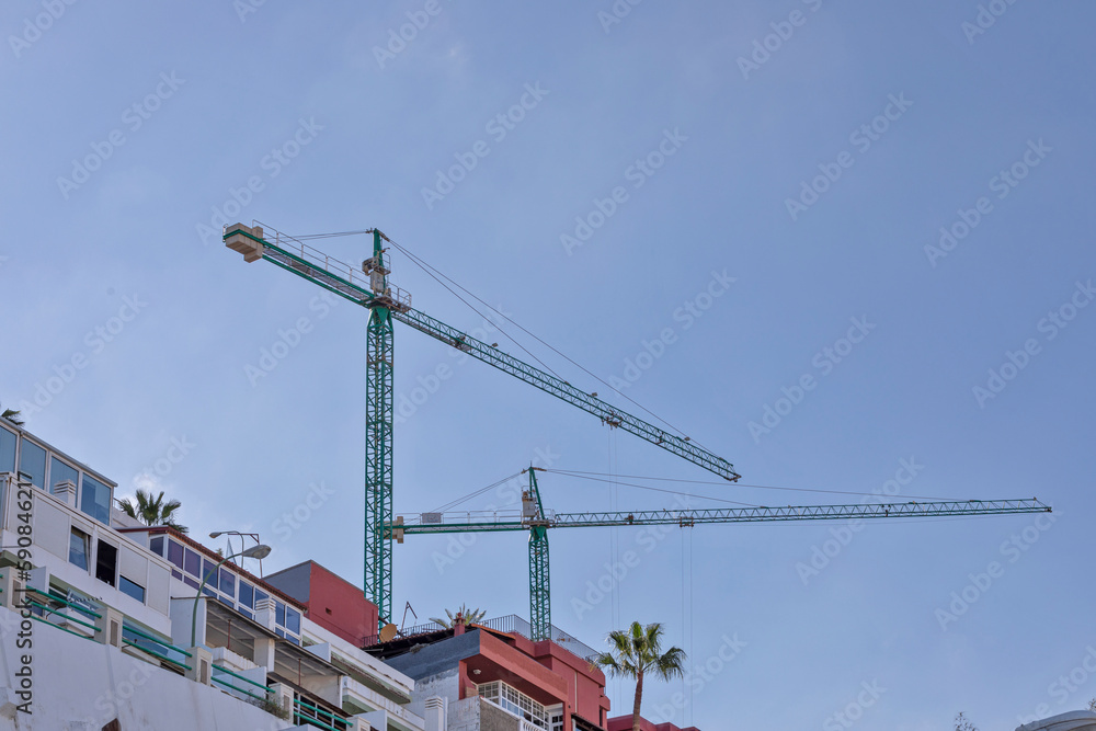 Two cranes tower above the roofs of a group of houses.