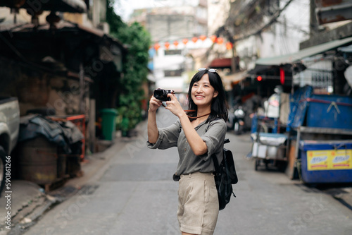 Young Asian woman backpack traveler using digital compact camera, enjoying street cultural local place and smile. Traveler checking out side streets.