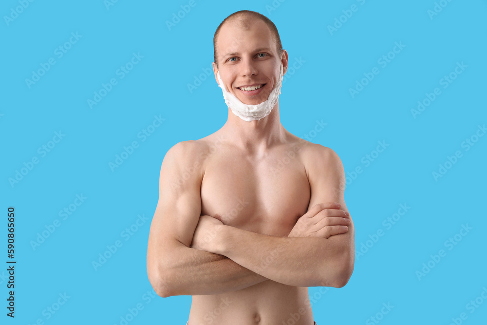 Young man with shaving foam on face against light blue background