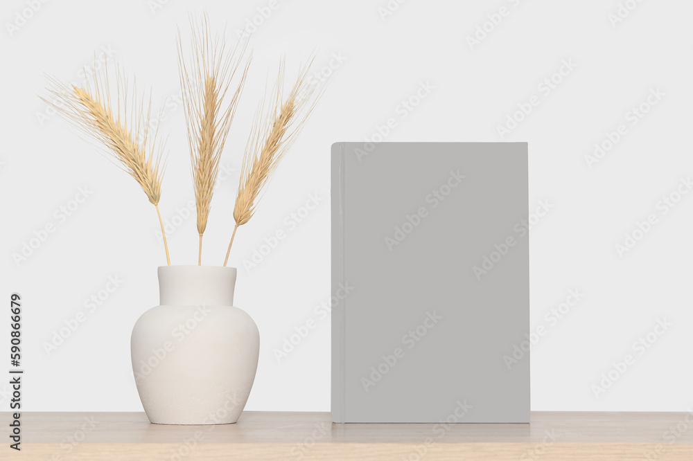 Mock-up of a gray book and a gray vase with dry branches of wheat.