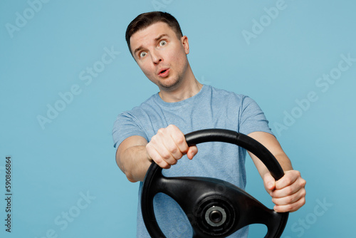 Young stupefied indignant puzzled shocked sadman wear casual t-shirt hold steering wheel driving car look camera isolated on plain pastel light blue cyan background studio portrait. Lifestyle concept.