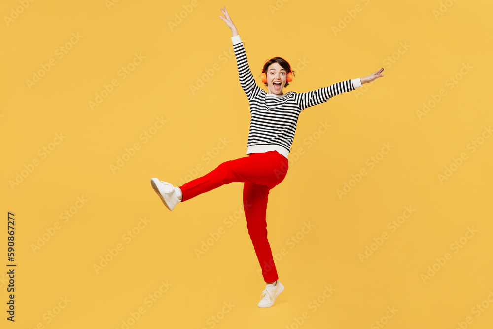 Full body young vivid happy woman wear casual striped black and white shirt headphones listen to music in headphones dance have fun isolated on plain yellow color background studio. Lifestyle concept.