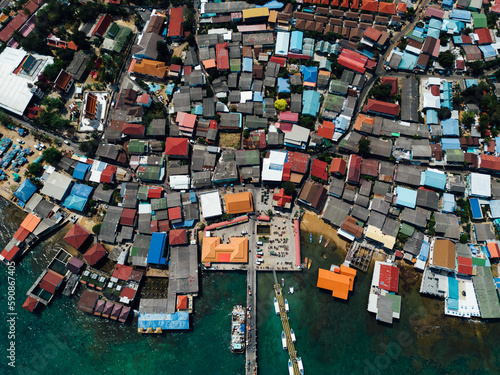 A bird's eye view of a ship navigating fishing boats moored to the docks, with village houses sprawling between the harbor
