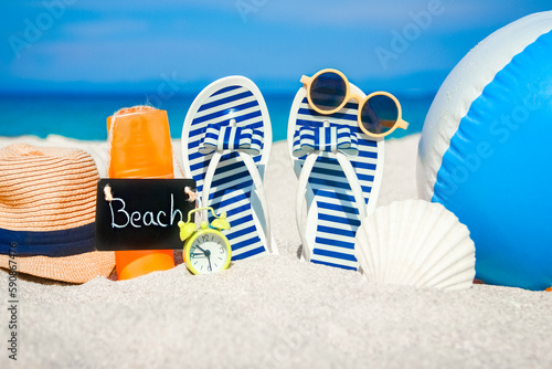 A Beach summer holiday banner background. Flip-flops and hat with a board and ball on the sand near the ocean. Summer accessories on the seashore. Tropical vacation and relax travel concept. 
