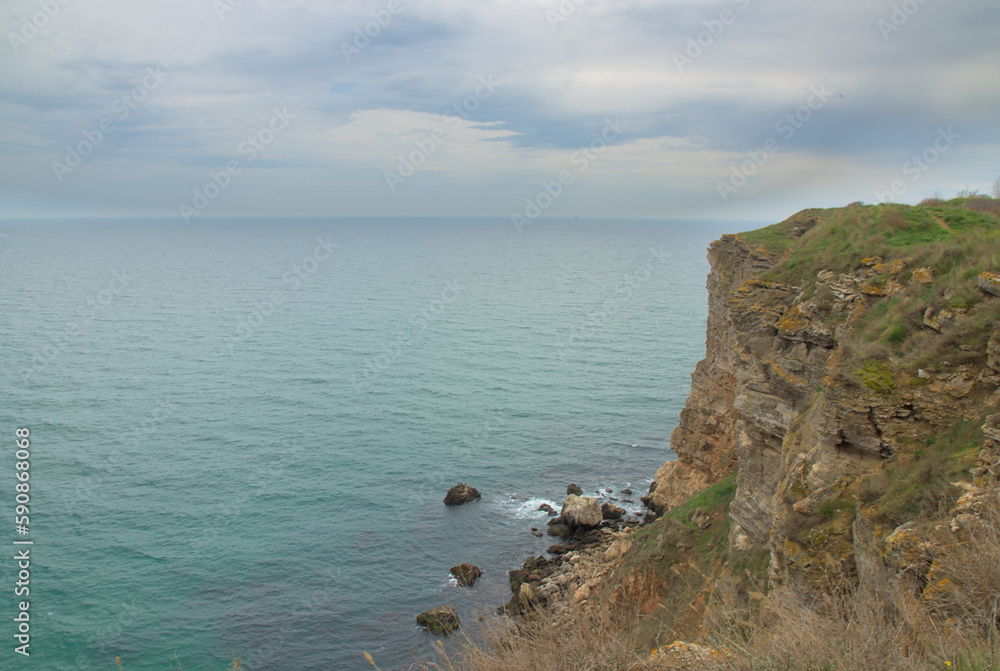 Turquoise sea and a rock with a green glade against the background of heavy rain clouds in early spring Turquoise sea and a rock with a green glade against the background of heavy rain clouds in early spring
