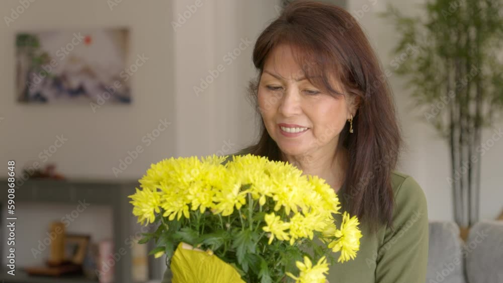 Closeup attractive middle age woman smiling looking at bouquet of yellow flowers in front of her Closeup attractive middle age woman smiling looking at bouquet of yellow flowers in front of her