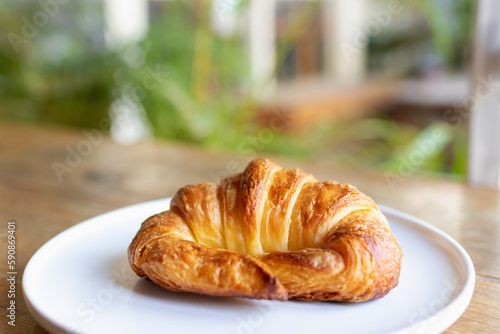 French croissant on white plate on wooden table and nature sunlight with shadow through from window.